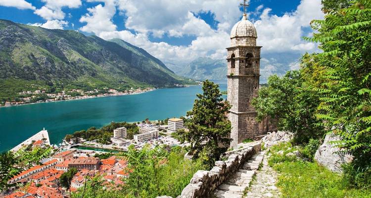 Une tour d'église dominant une ville côtière avec une mer bleue et des montagnes.