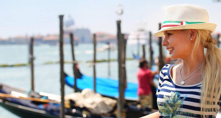 Femme souriante en chemise rayée et chapeau à côté de gondoles sur un canal vénitien ensoleillé