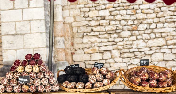 Une variété de saucisses présentées sur un étal de marché avec un mur de pierre.