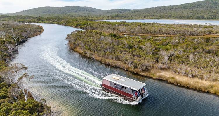Vista aérea de una casa flotante roja navegando por un río sinuoso rodeado de bosque en Australia Occidental.