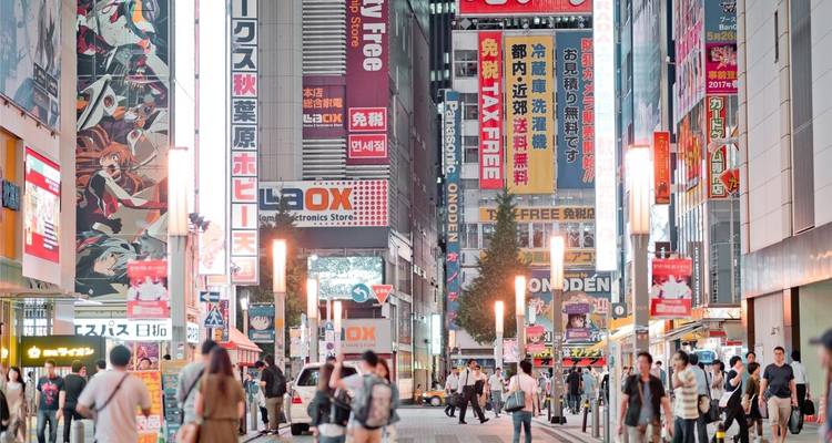 Una calle peatonal bulliciosa en Akihabara llena de tiendas de electrónica coloridas y carteles de anime bajo luces brillantes.