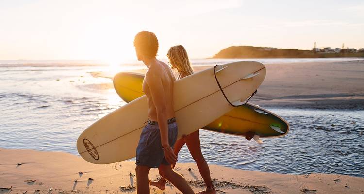Twee surfers die langs het strand lopen met surfplanken bij zonsondergang.