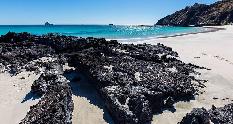Zwarte vulkanische rotsen op een ongerept strand met helder blauw water.