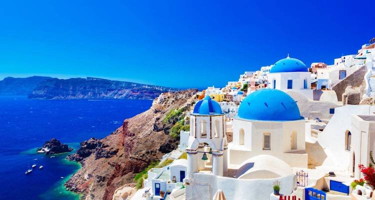 Iconic white buildings with blue domes on a hillside overlooking the sea.