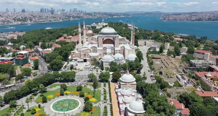 Vue aérienne d'une zone historique avec une mosquée proéminente, entourée d'une végétation luxuriante et d'un plan d'eau en arrière-plan.