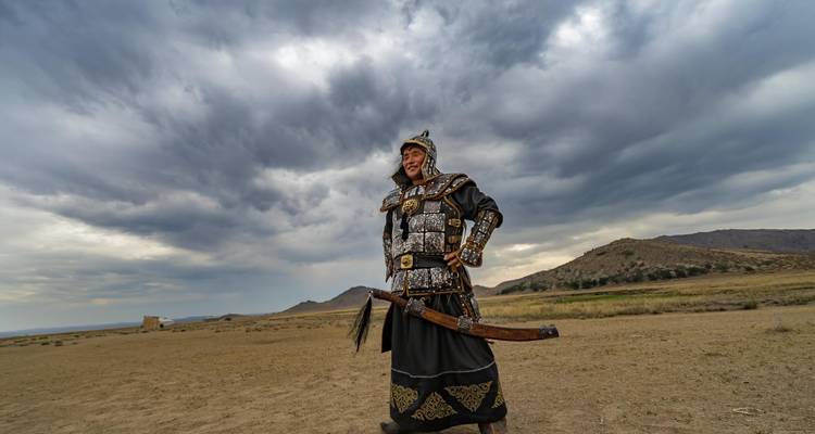 Personne en tenue traditionnelle de guerrier mongol dans un paysage désertique.