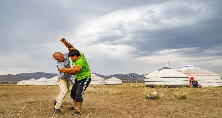 Deux personnes se livrent à un combat de lutte traditionnelle mongole près de yourtes.
