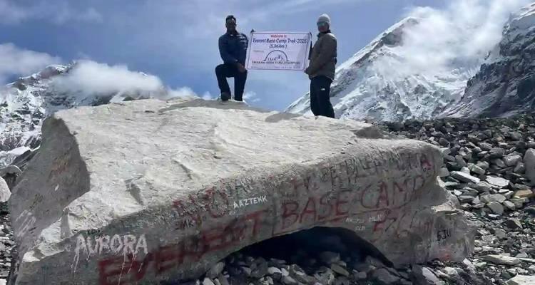 Vue lointaine de randonneurs debout sur un gros rocher marqué Camp de base de l'Everest.