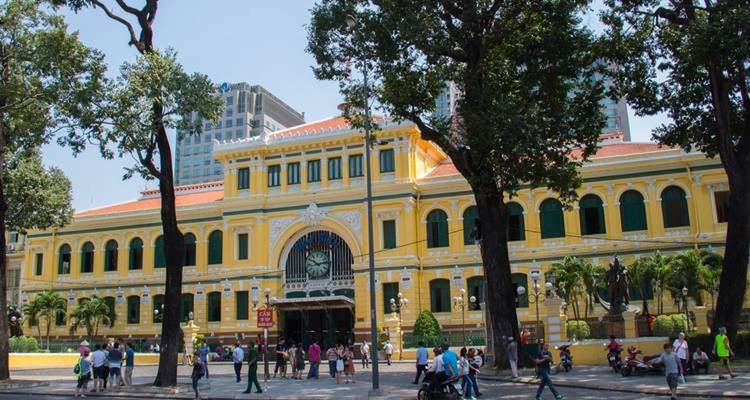 Yellow colonial building with people walking, seen from a street perspective.