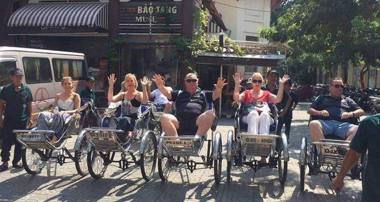 Tourists on trishaws waving to the camera on a city street.