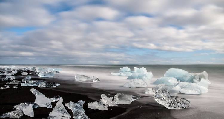 Playa de arena negra con trozos de hielo dispersos y cielo nublado.