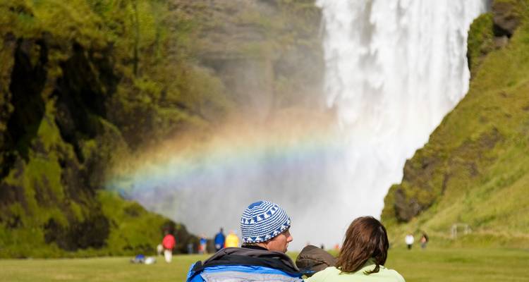 Un couple assis près d'une cascade avec un arc-en-ciel visible.