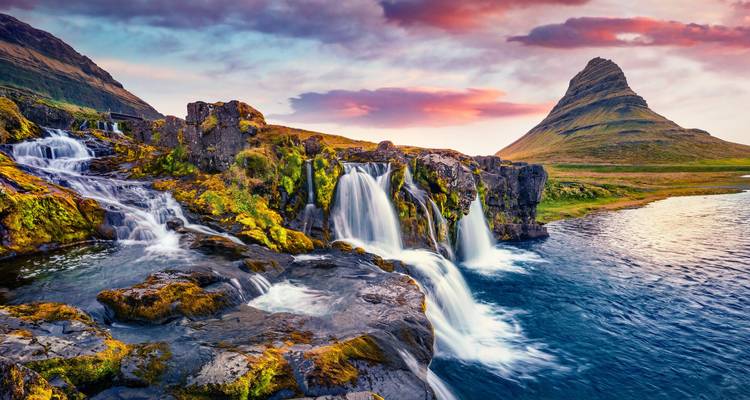 Vue spectaculaire des chutes d'eau de Kirkjufellsfoss s'écoulant sous des rochers couverts de mousse avec la montagne Kirkjufell au coucher de soleil coloré.