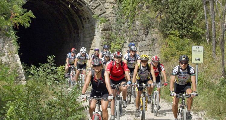 Group of cyclists riding near a stone tunnel.