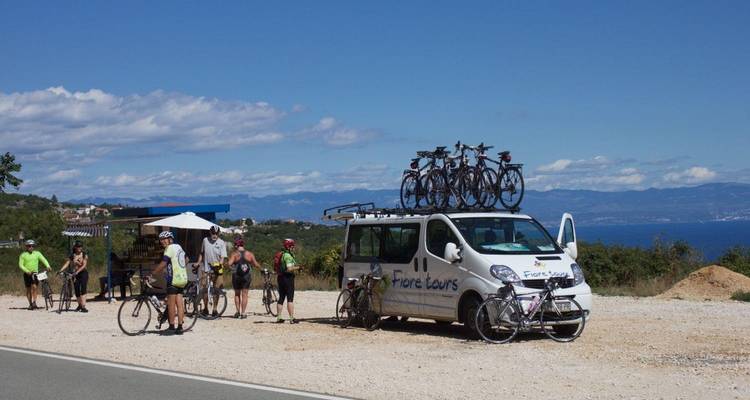 Cyclists resting by a van with bikes against the backdrop of the sea.
