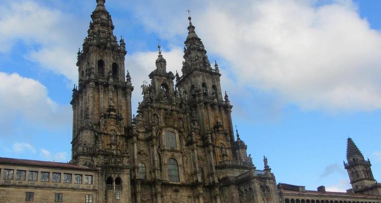 Façade ornée à tours jumelles de la cathédrale de Saint-Jacques-de-Compostelle sur fond de ciel partiellement nuageux.