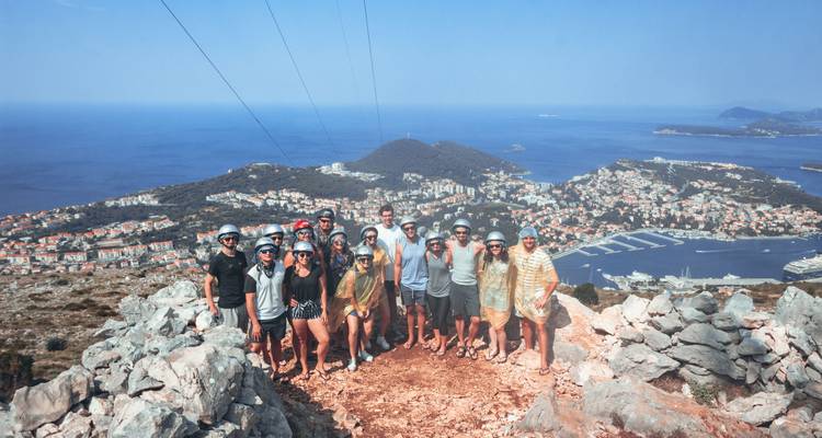 Grupo de excursionistas posando en la cima rocosa de una colina con vistas a la ciudad costera y la marina muy abajo