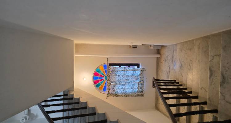 Escalera de mármol sencilla con una ventana arqueada de vidrieras coloridas.