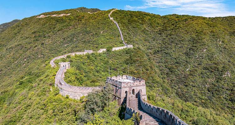 Een stuk van de Grote Muur dat zich slingerend uitstrekt over groene bergkammen onder een helderblauwe hemel.