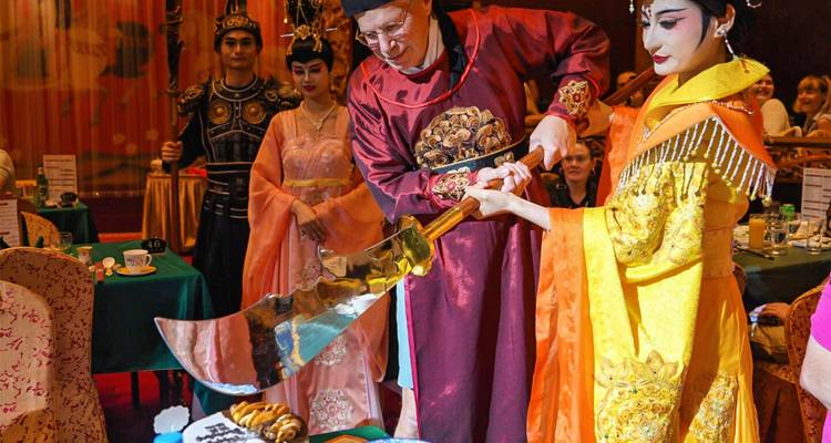Dinnershow in kostuum waarbij een performer in keizerlijke kleding brood snijdt met een overgrote zwaard voor de gasten.