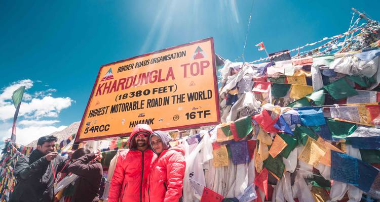 Gruppe von Menschen auf dem Khardungla Top mit Gebetsfahnen und einem Schild.