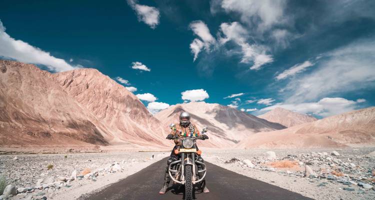 Eine Person fährt auf einem Motorrad auf einer Straße in einer bergigen Wüstengegend.