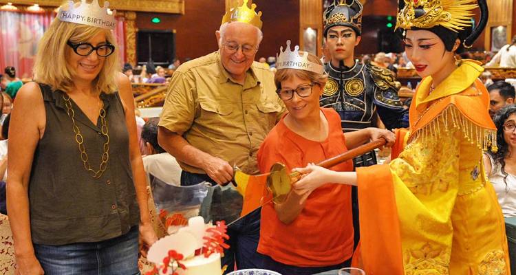 Celebración de cumpleaños durante un espectáculo tradicional de cena china con artistas disfrazados ayudando a los huéspedes a cortar el pastel.