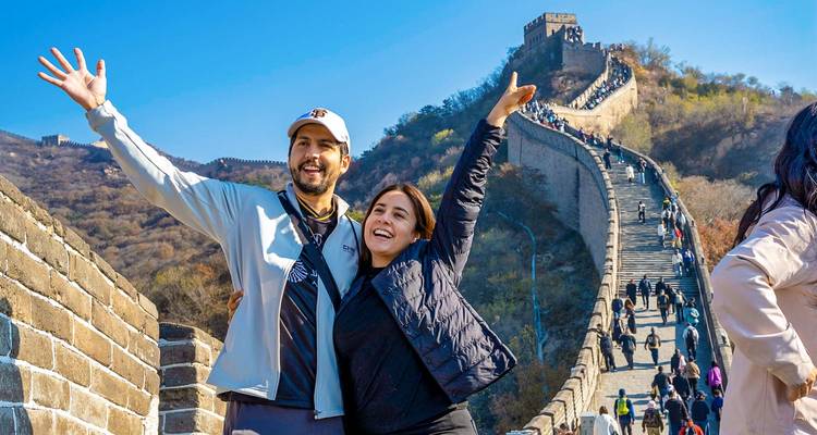 Pareja feliz posando en la Gran Muralla de China con un hermoso telón de fondo montañoso y murallas sinuosas.