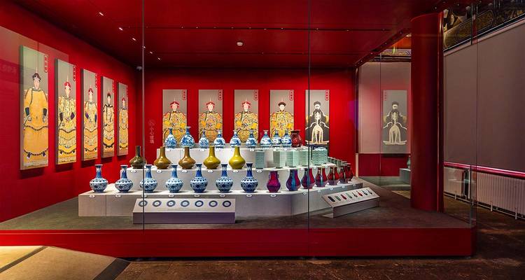 Galería de museo elegante con paredes rojo vibrante que exhibe filas de jarrones de porcelana y retratos de la realeza china.