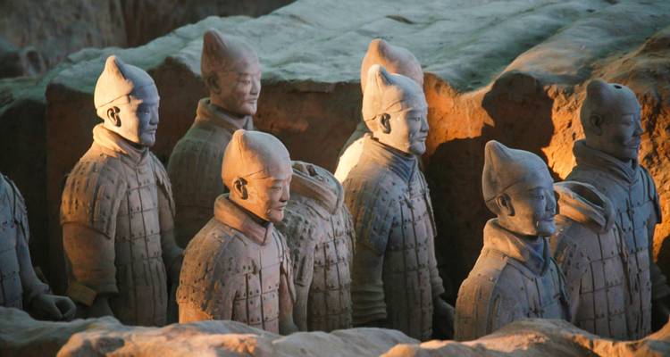 Fila de estatuas de Guerreros de Terracota de tamaño natural iluminadas dentro del foso de excavación.