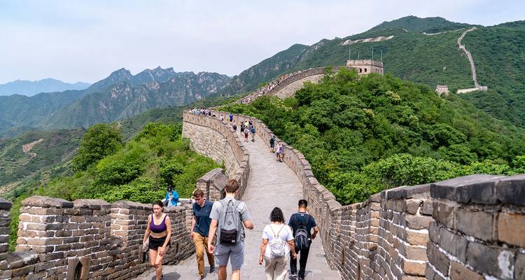 Les randonneurs marchent le long des remparts de pierre de la Grande Muraille de Chine qui serpente sur les montagnes verdoyantes.