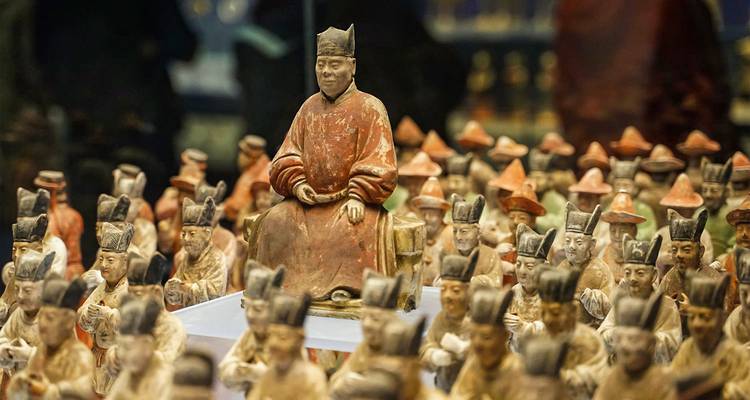 Exposition de petites figurines anciennes dans un musée avec une figure centrale assise en évidence.