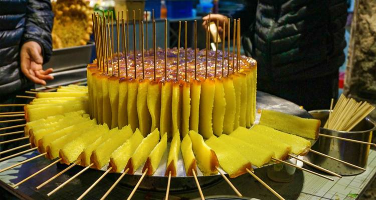 Plateau rond de gâteau de riz gluant jaune vif tranché sur des brochettes à un stand de nourriture de nuit animé.