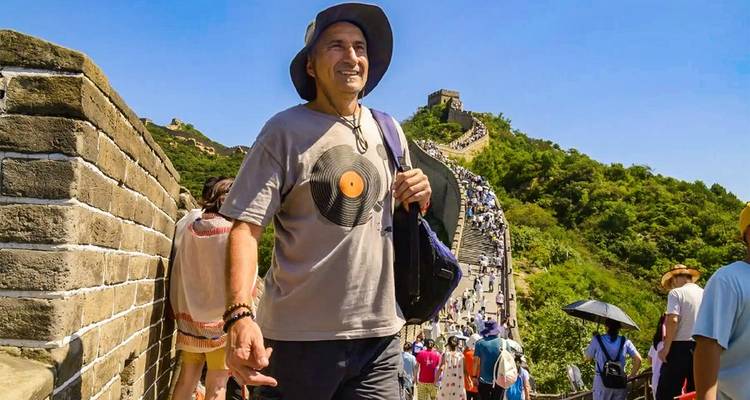 Un visitante caminando por la Gran Muralla en un brillante día de verano mientras una corriente de turistas sigue los escalones de piedra.