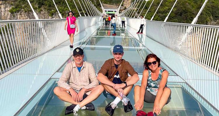 Turistas sentados en un puente colgante de cristal muy arriba de los cañones boscosos en Zhangjiajie.