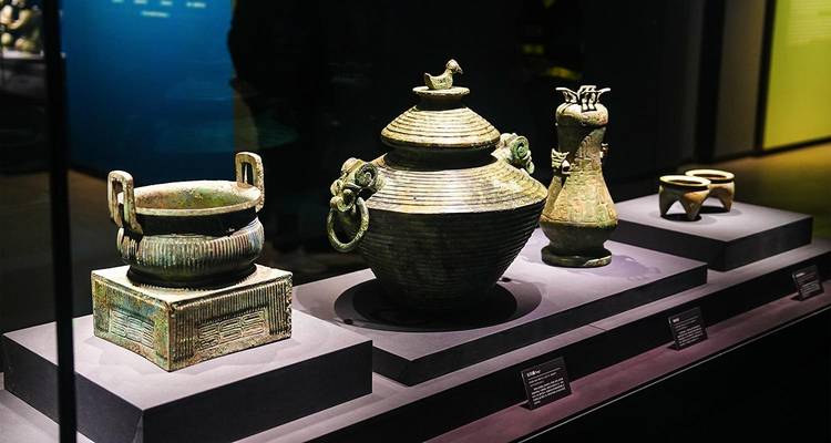 Exhibición de antiguos vasos rituales de bronce expuestos bajo la iluminación del museo dentro de una vitrina de cristal.