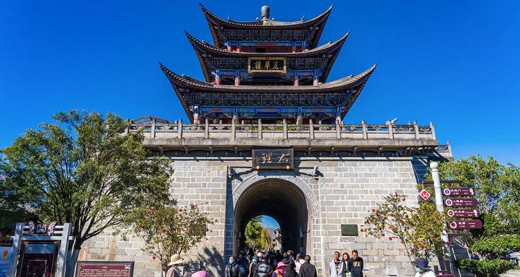 Visitors enter an ancient multi-tiered gate tower under a vivid blue sky in a historic walled town.