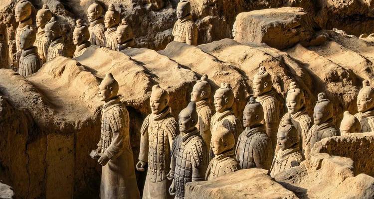 Rangées en gros plan des guerriers de l'Armée de terre cuite se tenant dans des fosses excavées sous une lumière chaleureuse.