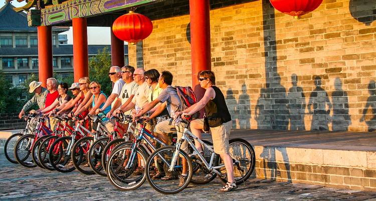 Groupe de personnes avec des vélos devant des murs anciens.