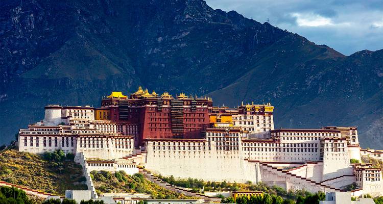 Het majestueuze Potala Palace rijst op tegen een achtergrond van ruige Himalayaanse bergen onder dramatische luchten.