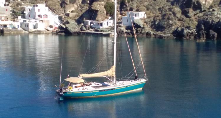 Voilier ancré sur une côte rocheuse avec des maisons.