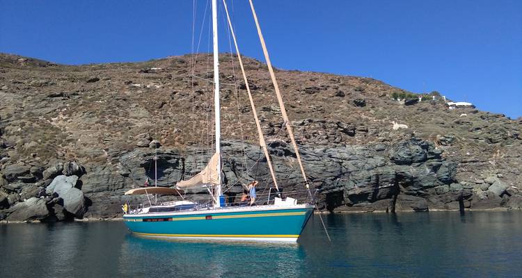 Sailing yacht docked near a rocky shore with clear blue sky.