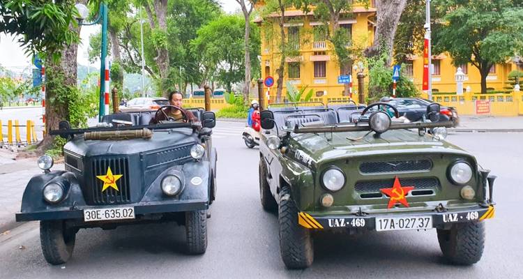 Deux véhicules militaires vintage garés dans une rue avec un conducteur visible.