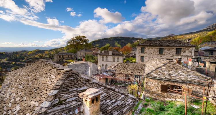 Casas tradicionales con tejados de piedra de un pueblo de montaña bajo un cielo brillante con colinas onduladas y follaje otoñal.