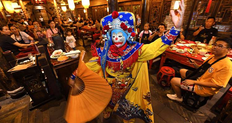 Performeur d'opéra du Sichuan changeant de masque en costume éclatant divertissant les clients dans un restaurant animé.
