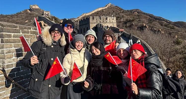 Un pequeño grupo de turistas abrigados con abrigos de invierno agita orgullosamente banderas chinas en la cima de la Gran Muralla bajo un cielo azul despejado.