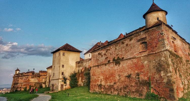 Fortified walls and towers of a historical site with people walking nearby.