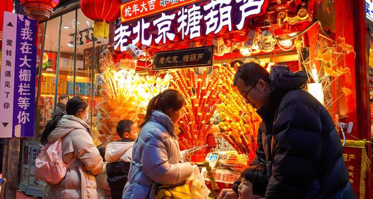 Une famille choisit des bonbons traditionnels dans une confiserie de Pékin bien éclairée, décorée de lanternes rouges.
