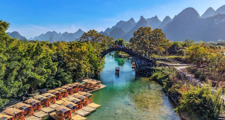 Malerische Steinbogenbrücke über einen ruhigen Fluss, umgeben von Karstgipfeln und Bambusflößen in Yangshuo.