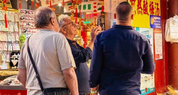 Drei Reisende untersuchen bunte Waren an einem belebten Verkaufsstand auf einem chinesischen Straßenmarkt.